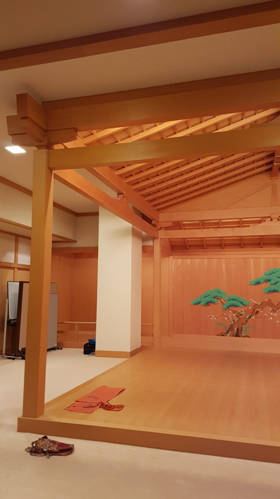 A slightly raised noh stage, complete with pillars, roof, and mirror board, on a carpeted floor