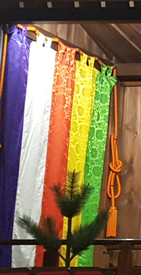 A silk curtain with purple, white, red, yellow, and green vertical stripes with red ropes tied in ornate knots on either side