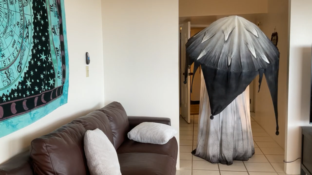 A person in a giant mushroom costume stands down a hallway at the threshold of a living room