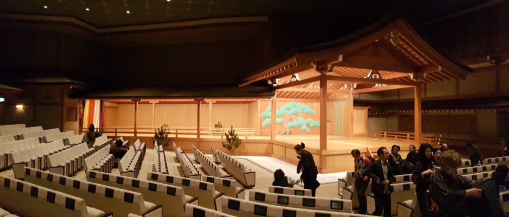 Audience seats at along the front and side of the nogaku stage with small screens for title viewing.