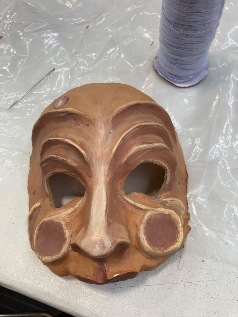 A half mask with exaggerated wrinkles above the eyes, circles on the cheeks and a bump in the forehead.