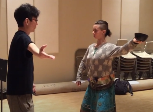 Shigeyama Sennojō III instructs a UHM student who mirrors him holding a bowl in an outstretched arm